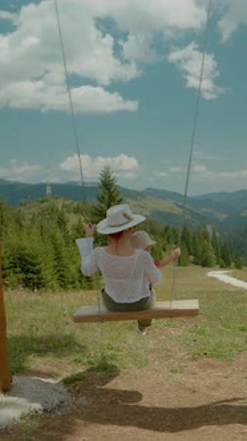 Vertical video Young mother swings her child amidst beautiful mountain landscape