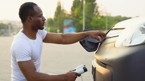 African American Man Charging Cargo Electric Car Near Warehouse Green Energy Eco Friendly Fuel