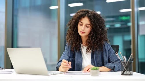 Businesswoman Working on Laptop and Taking Notes in Modern Office