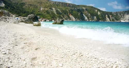 Clear sea waves splashing on peaceful white beach with pebbles, seascape with rocks in background