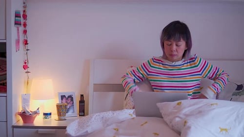 Young Adult Woman Works on Laptop in Bed