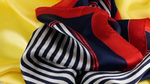A light silk scarf in blue, white and red stripes falls in soft folds slowly on a bright yellow silk