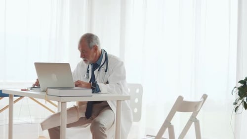 Senior Doctor with Laptop Working at the Office Desk