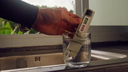 Vue à la première personne de la main mesurant la pureté de l'eau potable avec un testeur numérique montrant vingt