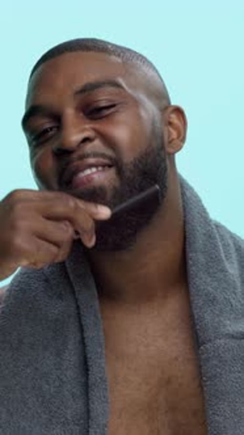 Man Combs Beard with a Towel around his Shoulders