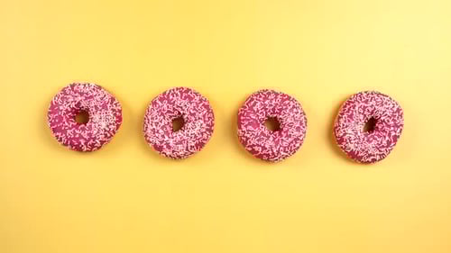 Colorful Donuts Being Grabbed on Yellow Background