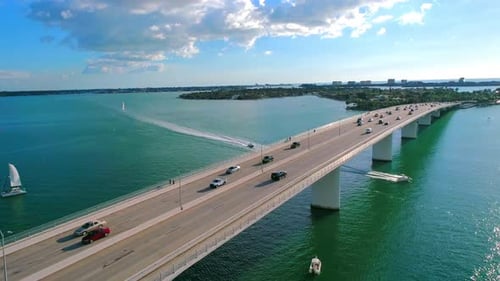 Following vehicle traffic over a water bridge in a tropical setting while boats pass underneath brid