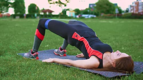 Woman Does Glute Bridge With Resistance Band Outdoors