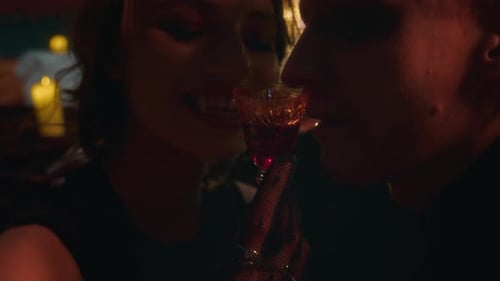 Close-up of Vampire Woman Offering Glass of Blood to Man in Intimate Manner