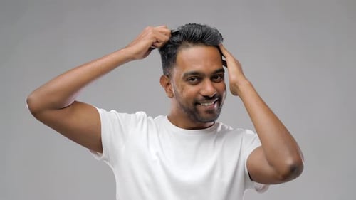 Smiling man combs his hair in studio setting
