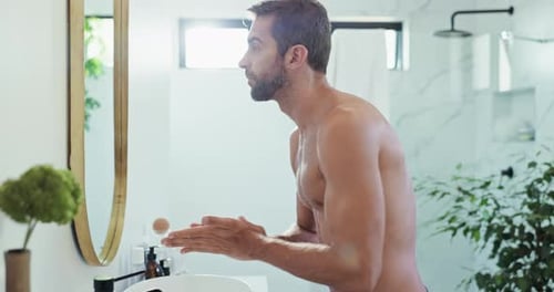 Man Applies Lotion to Face in Modern Bathroom