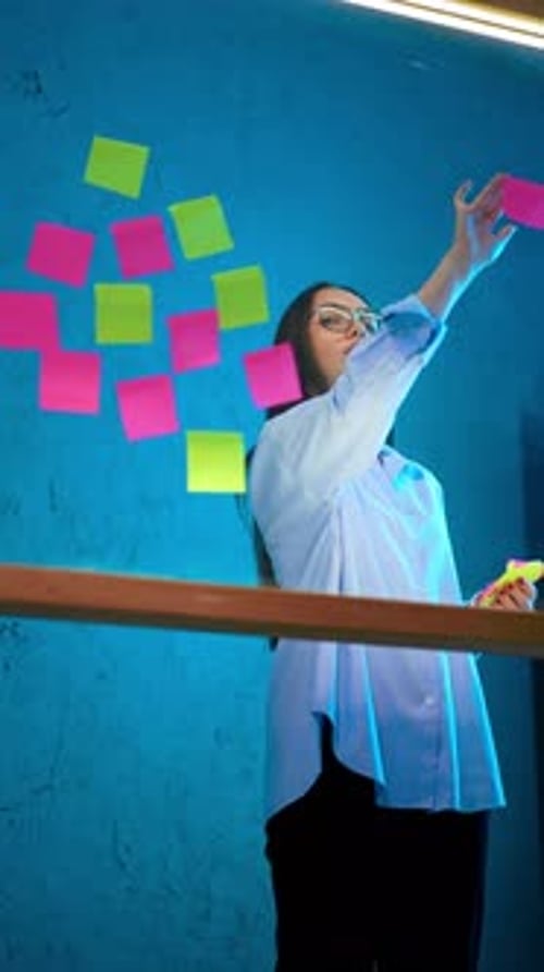 Lady in white shirt and black trousers puts stickers on the glass wall.