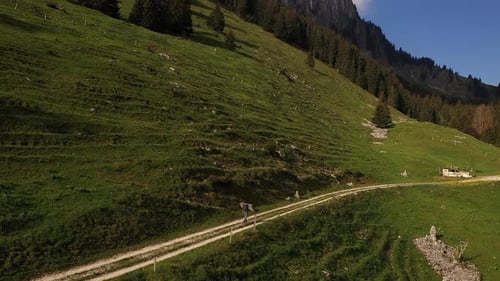Aerial drone shot, backpacker hiking on mountain cliffside dirt trail during summer