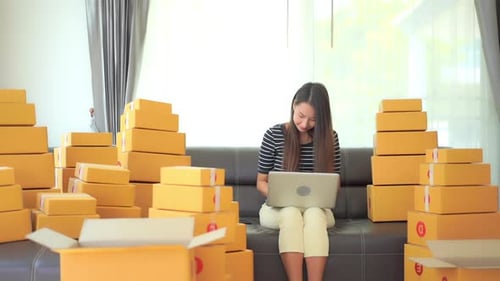 Woman with Laptop surrounded by Shipping Boxes at Home