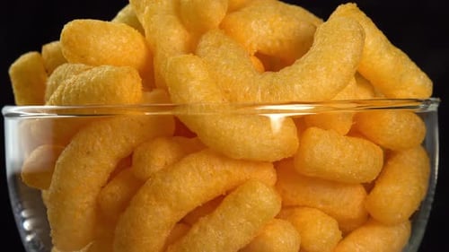 Corn cheese chips rotate in a glass bowl macro. Crispy cheese snack. Crispy fluffy corn sticks