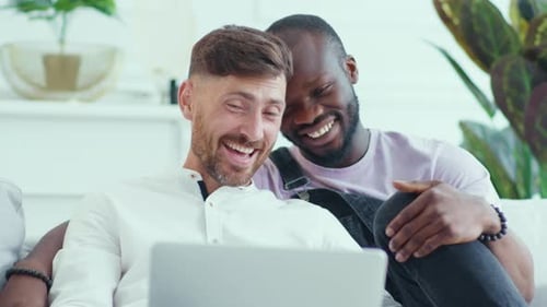 Happy Male Couple Laughing Together Using Laptop at Home