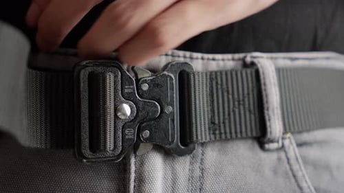 Ceinture tactique noire à attacher et à boucler avec les mains sur un jean gris, gros plan