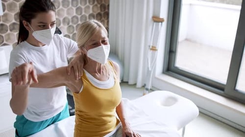 Woman Physical Therapist Assists Senior Woman with Arm