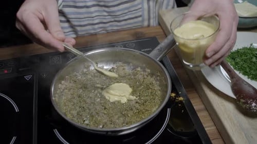 A chef puts yellow mustard into a metal pan. Preparing delicious café de paris sauce for steaks.