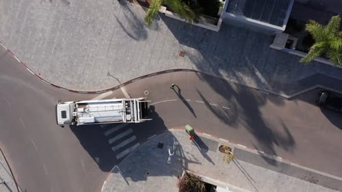 Municipal garbage truck at work, loading green trash cans.