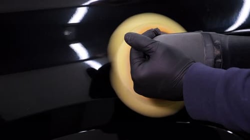 A Man Polishes a Black Car with a Car Polishing Machine at a Car Dealership