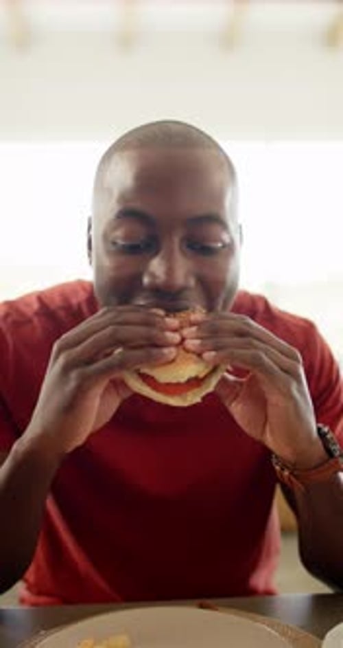 Vertical video: Eating burger, man enjoying meal at restaurant with fries on table