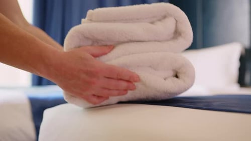 Female maid hands putting fresh white towels on bed in room close-up