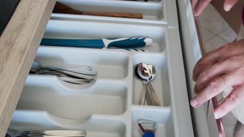 Hand opens kitchen drawer, selects scissors from organized cutlery compartment, then closes it.