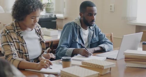 African American Students Man and Woman Studying in College Library Using Smartphone and Laptop