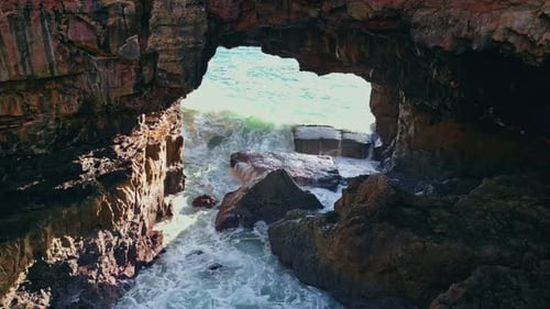 Huge ocean wave splashing on dark volcanic cliffs in super slow motion