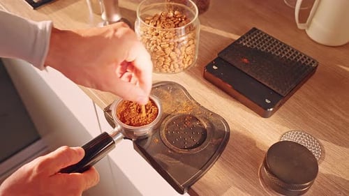 Barista Hand Leveling Ground Coffee in Portafilter with Wooden Stick on Countertop near Beans Jar