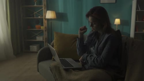 Tired Woman Working on a Laptop Studying Online While Sitting in a Room in the Dark Close Up