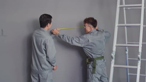 Couple of Construction Workers Measuring Wall