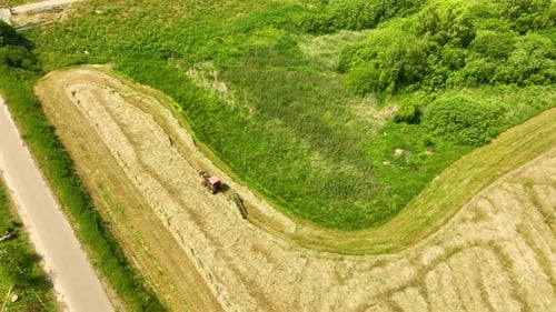 Aerial view of a tractor working in a field, creating rows of cut hay