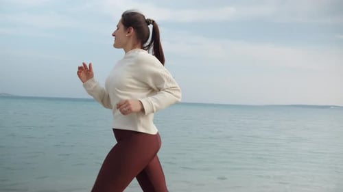 Slow motion of young woman staying fit and healthy by jogging on the sandy sea beach at sunset