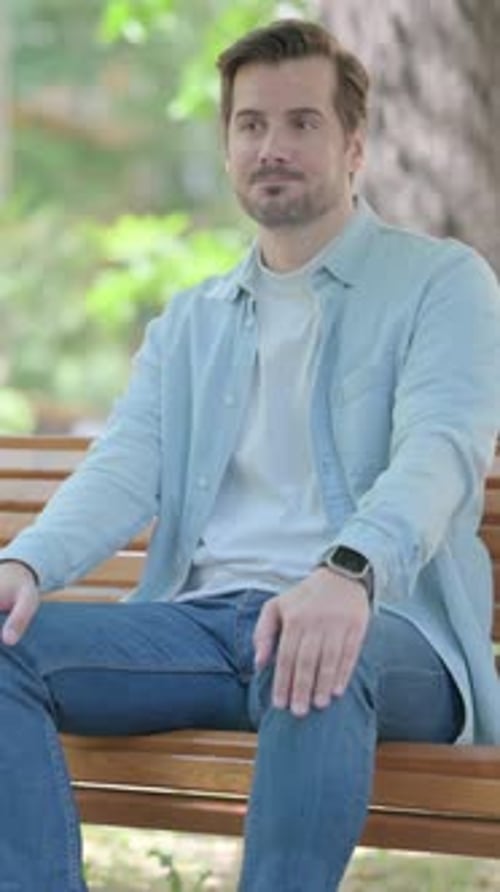 Man Sitting on Park Bench Looks at Watch