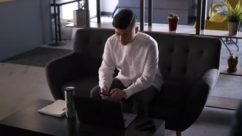 Man Using Smartphone on Couch in Modern Office