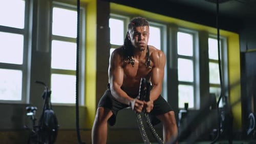 Muscular Man Exercising with Battle Ropes in Gym
