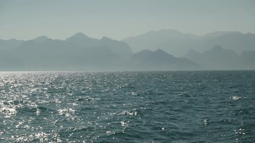 The sea on a sunny day, the mountains in the distance, a light haze on the water.