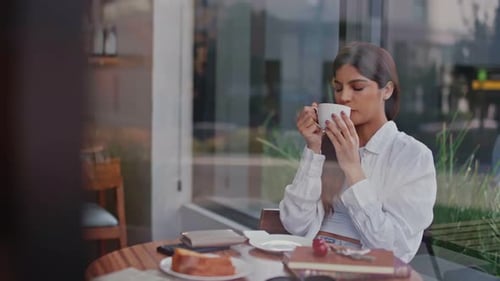 Woman Enjoying a Warm Coffee at a Sidewalk Cafe