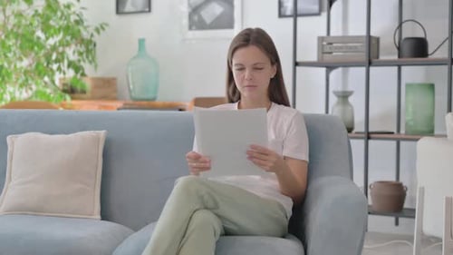 Woman Reads Paper Sitting on Sofa at Home