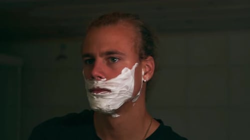 Young Man Shaving Face in Dark Bathroom