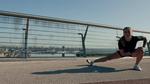 Fitness young sportswoman girl in the morning doing warm-up leg exercises before training on street