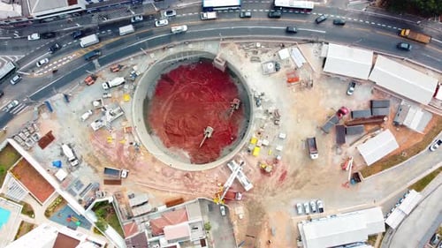 Excavación del pozo de lanzamiento para la construcción de una estación de metro que muestra una excavadora y automóviles por los alrededores