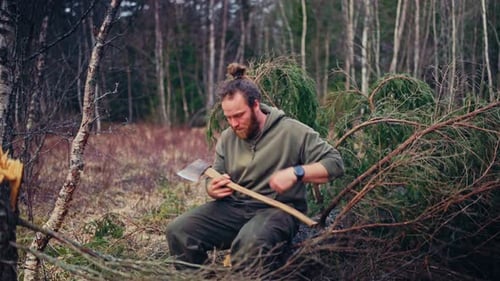 A Man Sharpening An Axe In The Woods. Static Shot