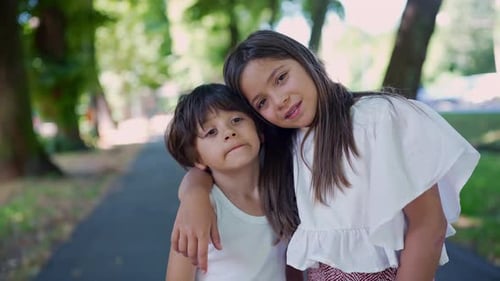 Young girl with her arm around a boy, tilting her head towards him as they stand on a park pathway.