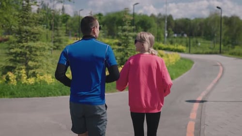 A Slender and Athletic Man and Woman Run Through a Landscaped City Park Sport in the Summer Allows