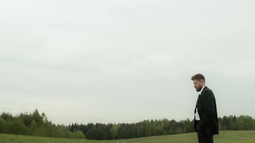 Man Stands Beside Coffin in Grassy Rural Field