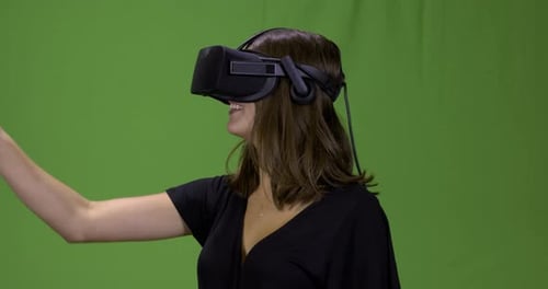 Young woman with a virtual reality head set on a green screen.