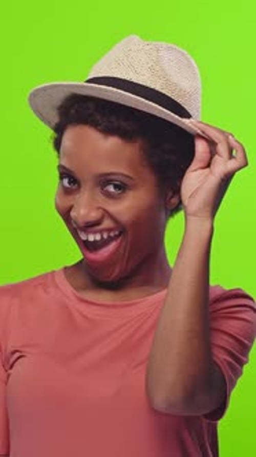 Jeune femme afro-américaine portant des chapeaux pose de manière ludique sur un fond coloré vert vif